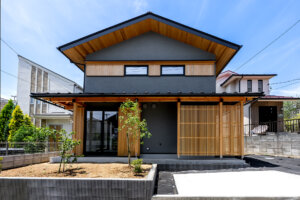 Modern two-story house with gray walls, timber accents, and a large sloped wooden roof under a blue sky.