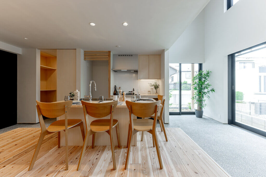 Open-plan kitchen and dining area with a wooden island, six chairs, and large glass doors bringing in natural light, plus a potted plant.