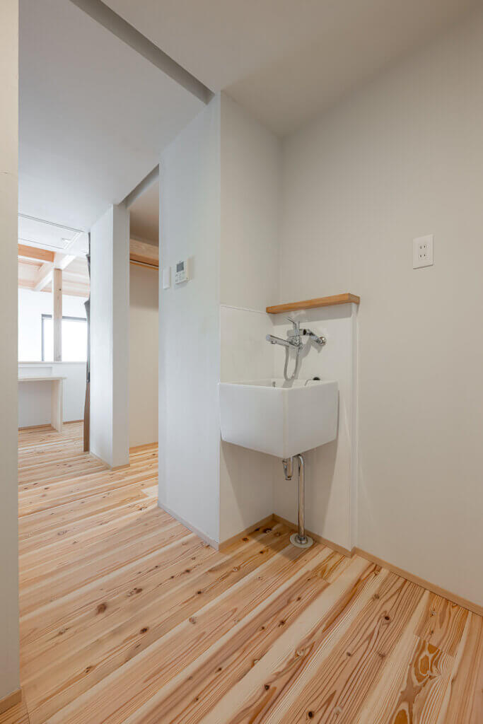 White wall-mounted utility sink with chrome faucet in a bright, minimalist hallway with light wood flooring and open doorways ahead.